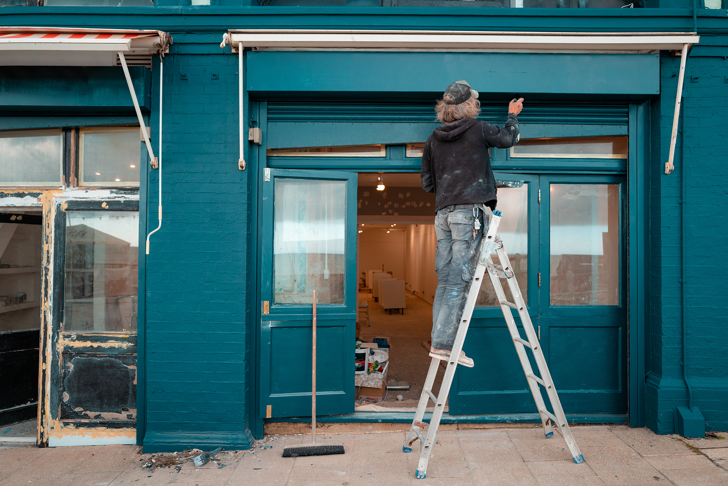 Person painting storefront exterior on ladder.