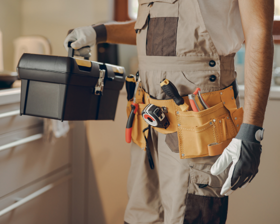 Worker holding toolbox and wearing tool belt.